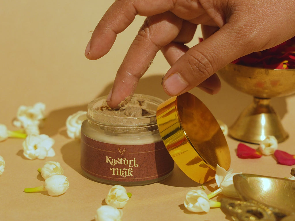 Hand taking a small amount of Deiveegaa Kasturi Tilak paste from the jar